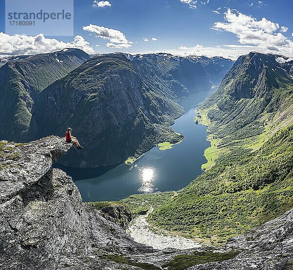 Wanderin sitzt auf Felszunge  Blick vom Gipfel des Breiskrednosi  Berge und Fjord  Nærøyfjord  Aurland  Norwegen  Europa