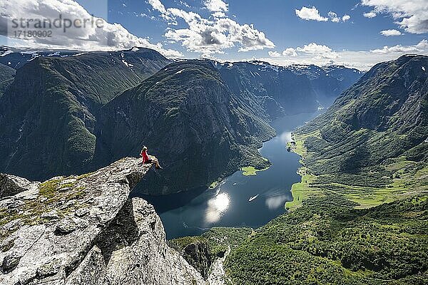 Wanderin sitzt auf Felszunge  Blick vom Gipfel des Breiskrednosi  Berge und Fjord  Nærøyfjord  Aurland  Norwegen  Europa