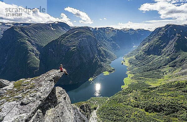 Wanderin sitzt auf Felszunge  Blick vom Gipfel des Breiskrednosi  Berge und Fjord  Nærøyfjord  Aurland  Norwegen  Europa