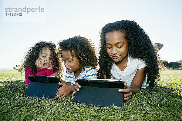 Junge gemischte Rasse Mädchen und ihr Bruder und Schwester mit zwei digitalen Tabletten  Bildschirmzeit