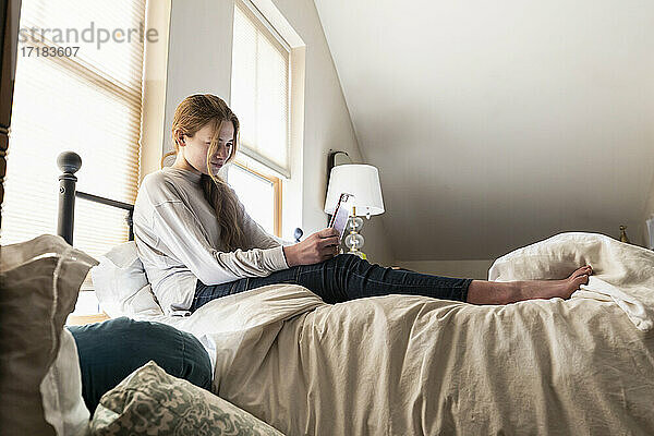 Teenager-Mädchen sitzt auf ihrem Bett und benutzt ihr Smartphone