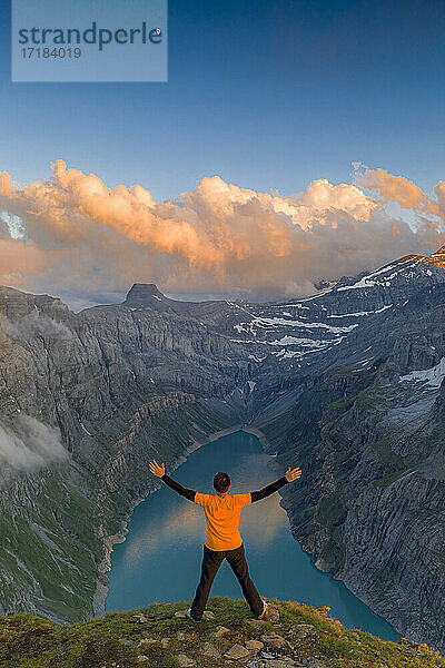 Mann mit ausgestreckten Armen genießt den Sonnenuntergang über dem Limmernsee  stehend auf einem Felsen  Kanton Glarus  Schweiz  Europa