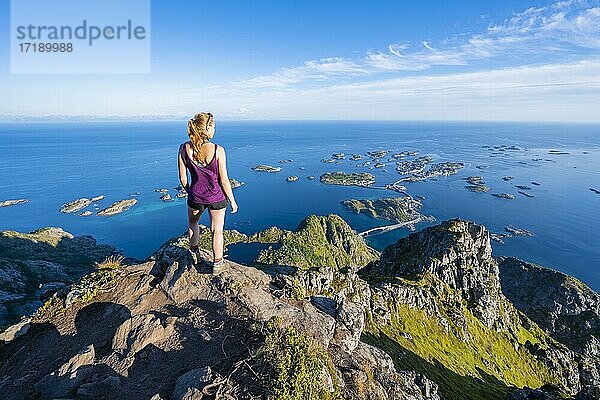 Kleine Felsinseln im Meer  Wanderin blickt vom Gipfel des Berges Festvågtind auf Ort Henningsvær  Vågan  Lofoten  Nordland  Norwegen  Europa