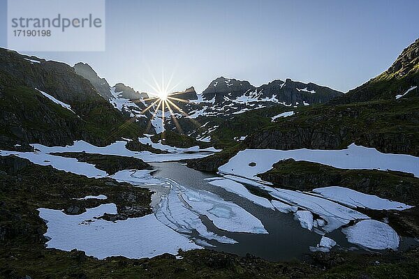 Sonne über See Isvatnet mit Eis  Berge und Schnee  an der Trollfjord Hytta  am Trollfjord  Lofoten  Nordland  Norwegen  Europa