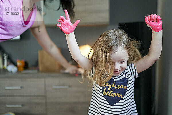 Glücklich lächelndes kleines Mädchen mit erhobenen Händen und bemalten Handflächen