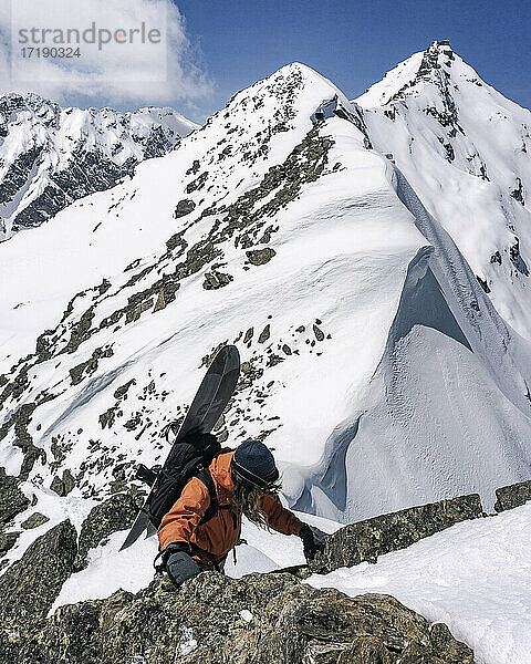 Mann mit Snowboard klettert auf einem schneebedeckten Berg im Urlaub auf Felsen