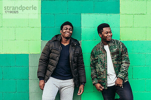 Porträt von zwei jungen schwarzen afroamerikanischen Jungen  die lächeln. Lehnt gegen grüne Wand Hintergrund.
