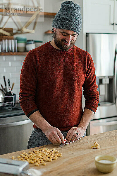 Ein glücklicher Koch macht Nudeln in seiner gemütlichen Metzgerblock-Küche.
