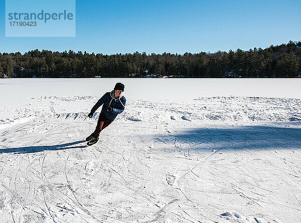 Ein Jugendlicher läuft an einem Wintertag in Kanada auf einem zugefrorenen See Schlittschuh.