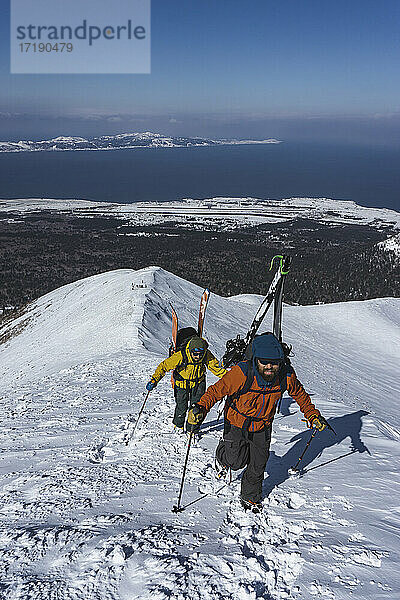 Menschen mit Skistöcken beim Klettern auf einen schneebedeckten Berg im Urlaub