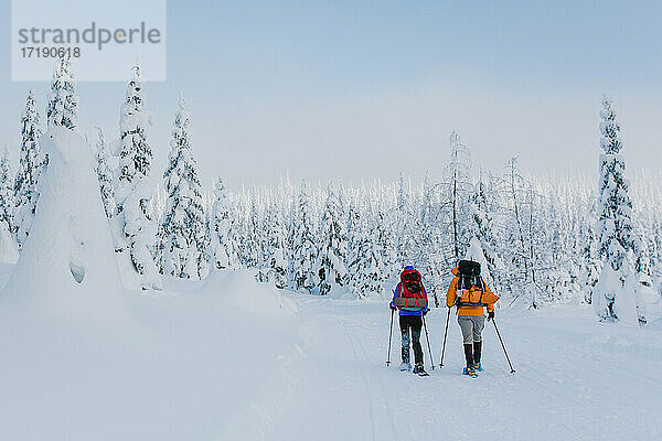 Zwei Freunde mit Rucksäcken und Trekkingstöcken bei Sonnenaufgang auf Schneeschuhen