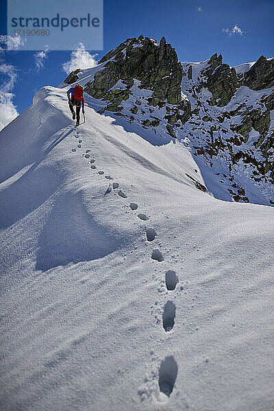 Ein Mann besteigt an einem sonnigen Tag einen verschneiten Berg in Devero  Italien.