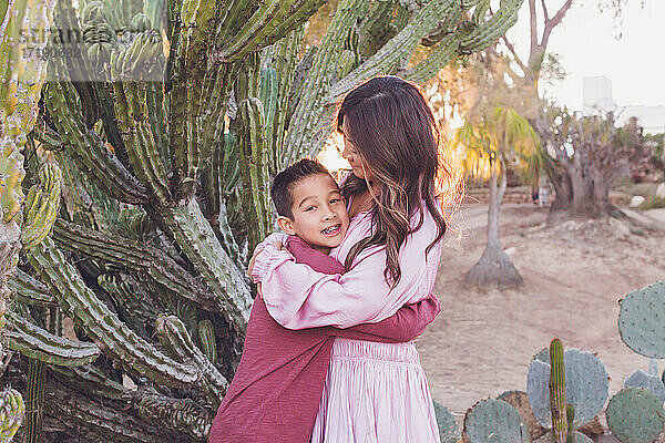 Mutter umarmt Sohn vor einem großen Kaktus mit Gegenlicht Sonne.