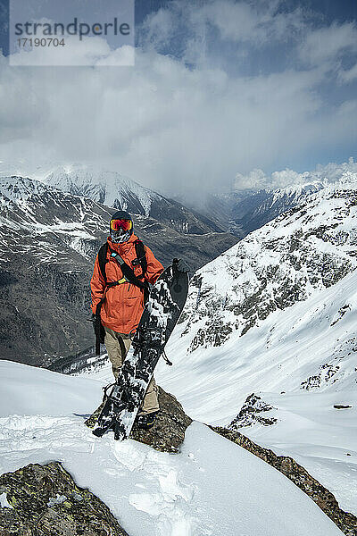 Mann mit Snowboard auf einem schneebedeckten Berg gegen den Himmel stehend