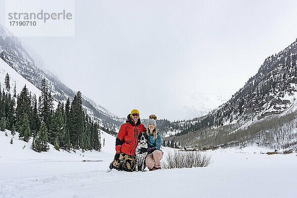 Glückliches Paar mit Vorstehhund auf schneebedecktem Feld gegen den Himmel im Urlaub