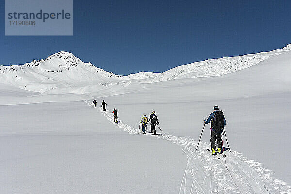 Rückansicht von Männern und Frauen mit Splitboards  die auf einem schneebedeckten Berg gegen den klaren Himmel laufen