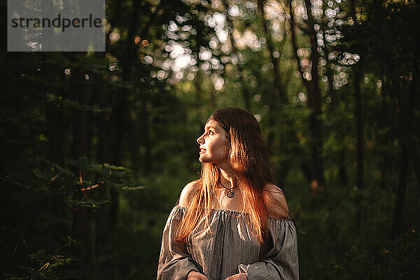 Junge Frau  die im dunklen Wald steht und das Sonnenlicht betrachtet