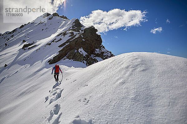 Ein Mann besteigt an einem sonnigen Tag einen verschneiten Berg in Devero  Italien.