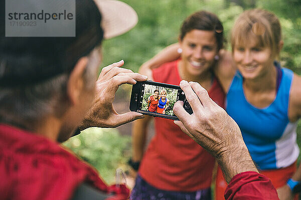 Drei Freunde laufen zusammen und halten an  um ein Foto mit dem Smartphone zu machen