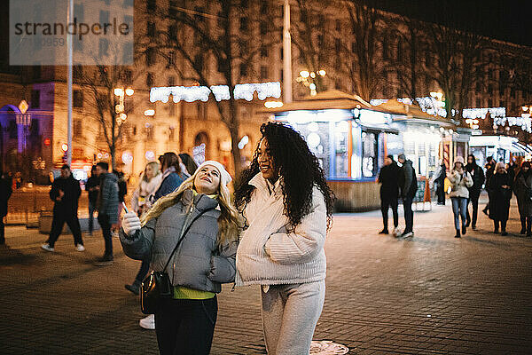 Glückliche weibliche Freunde gehen auf der Straße in der Stadt bei Nacht im Winter