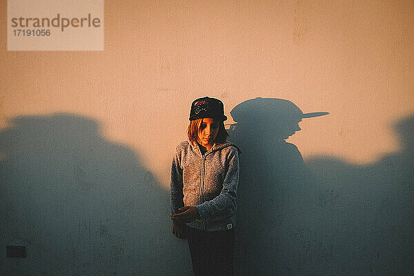 Junge steht bei Sonnenuntergang mit seinem Schatten an einer Wand