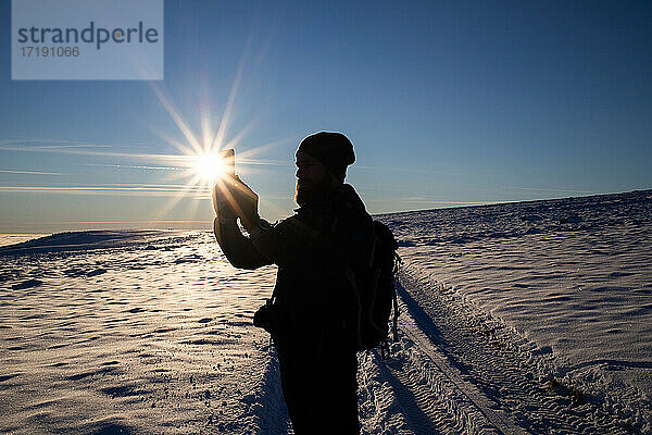 Mann wandert beim Fotografieren im Winter Sonnenuntergang