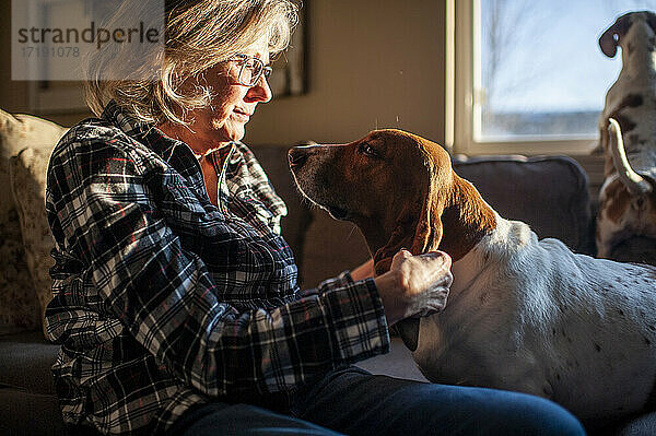 Glückliche Seniorin spielt mit Hundeohren auf der Couch zu Hause