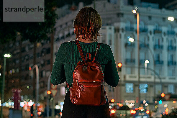 Rückenansicht einer jungen Frau mit Rucksack in einer nächtlichen Stadt