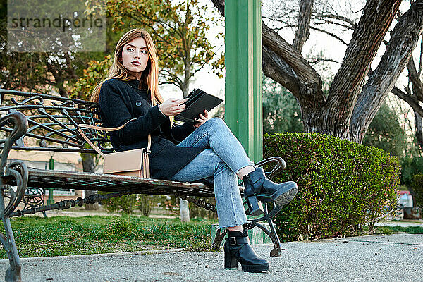 Eine attraktive junge Frau schaut in einem Park auf ihr Tablet