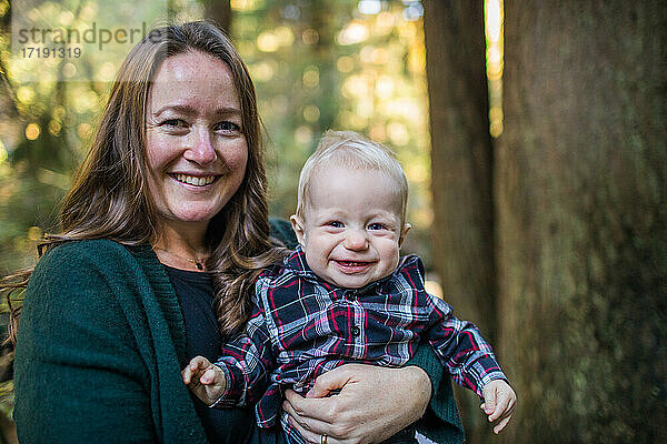 Porträt einer Mutter und eines kleinen Sohnes  die in einem Wald lächeln.