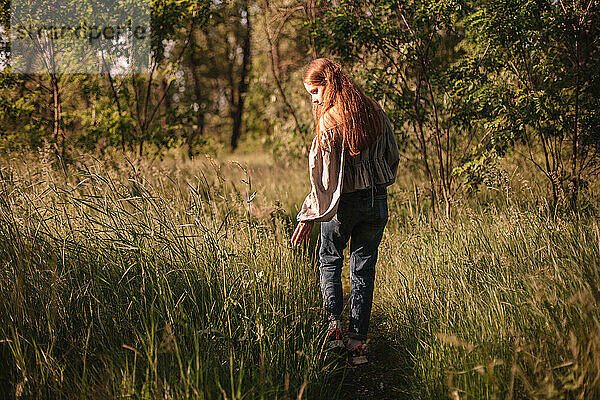Rückenansicht von Teenager-Mädchen berühren Gras zu Fuß auf dem Weg im Sommer