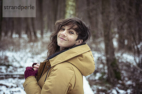 Fröhliche Frau lächelt frech über die Schulter im verschneiten Winterwald