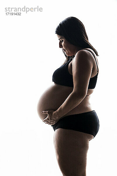 Seitenansicht einer schwangeren Frau auf weißem Hintergrund im Studio