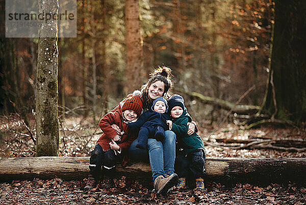 Mutter und Kinder sitzen glücklich lächelnd im Wald im Herbst