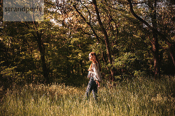 Teenager-Mädchen geht durch grünes Gras im Wald im Sommer