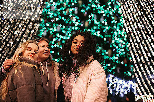Glückliche Freundinnen stehen nachts am Weihnachtsbaum in der Stadt