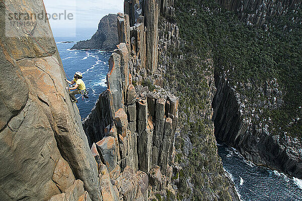 Junger Mann klettert an der exponierten Kante eines Felsrückens mit Säulen entlang der aus dem Meer ragenden Klippen in Cape Raoul  Tasmanien  Australien.