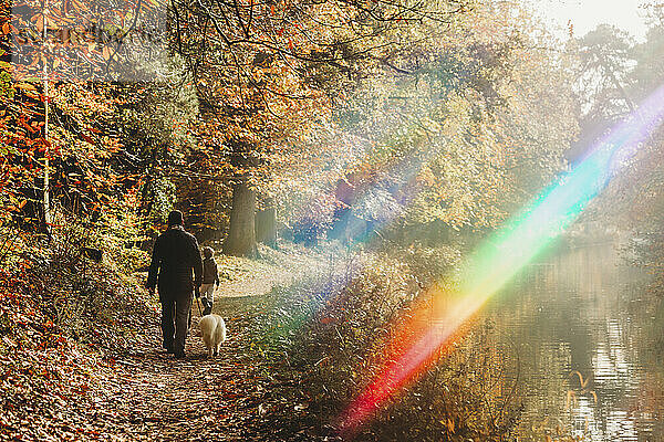 Mann  Kind und Hund spazieren mit Regenbogenfackel im Herbst auf dem Treidelpfad des Kanals