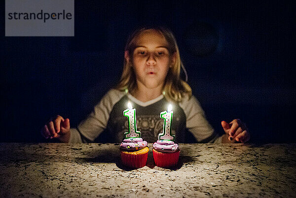 Tween Girl bläst Kerzen auf zwei Cupcakes aus  Gesicht nicht im Fokus