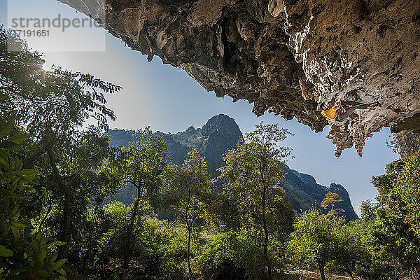 Mann klettert auf überhängendem Kalksteinfelsen in Laos