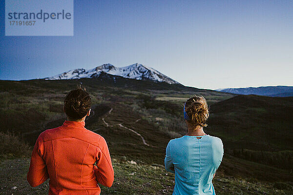 Zwei Freundinnen blicken in der Abenddämmerung gemeinsam auf einen Berg