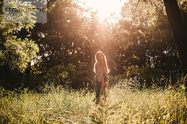 Junge Frau steht im Sommer im Gras im Wald