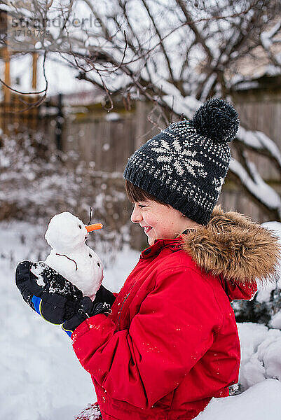 Junge hält an einem verschneiten Tag im Freien einen kleinen Schneemann in den Händen.
