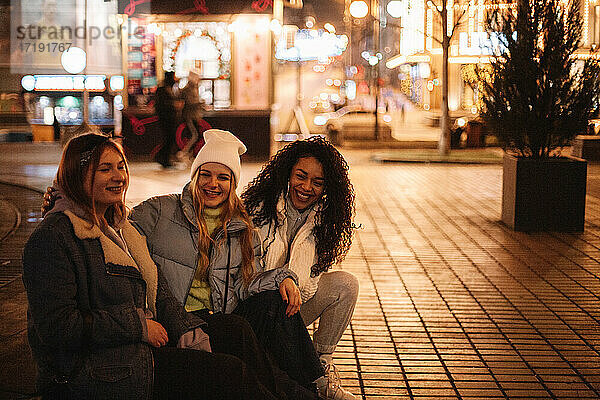 Glückliche Freundinnen sitzen auf der Straße in der Stadt bei Nacht