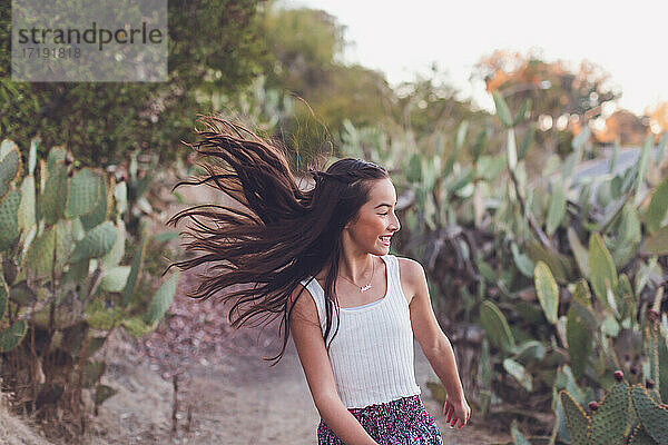 Gemischtrassiges Mädchen  das mit fliegenden langen Haaren über einen Kaktuspfad läuft.