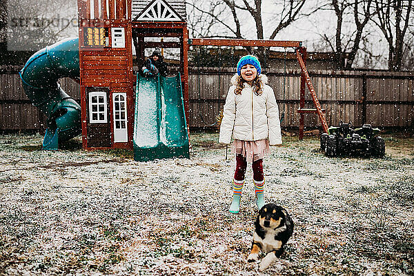Zwei kleine Kinder und ein Welpe spielen im Hinterhof an einem verschneiten Tag