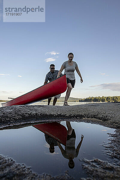 Mann und Frau  die sich in einer Pfütze spiegeln  ziehen ein rotes Kanu aus einem See in Maine