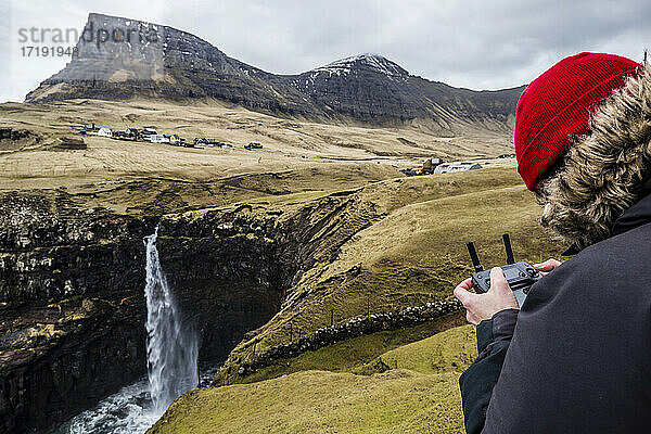 Pilot fliegt mit seiner Drohne (uav) über dem Mulafossur-Wasserfall auf der Insel Vagar auf den Färöern