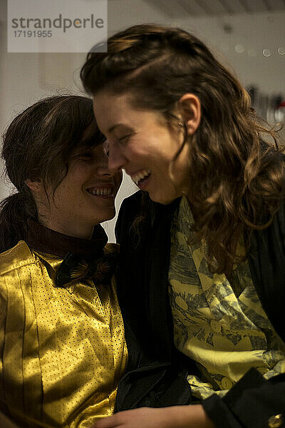 Queer lesbisches Paar lacht zu Hause im Küchensessel bei einer Dinnerparty