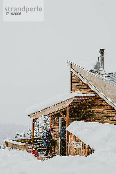 Zwei Freunde betreten eine rustikale Hütte  während es draußen schneit